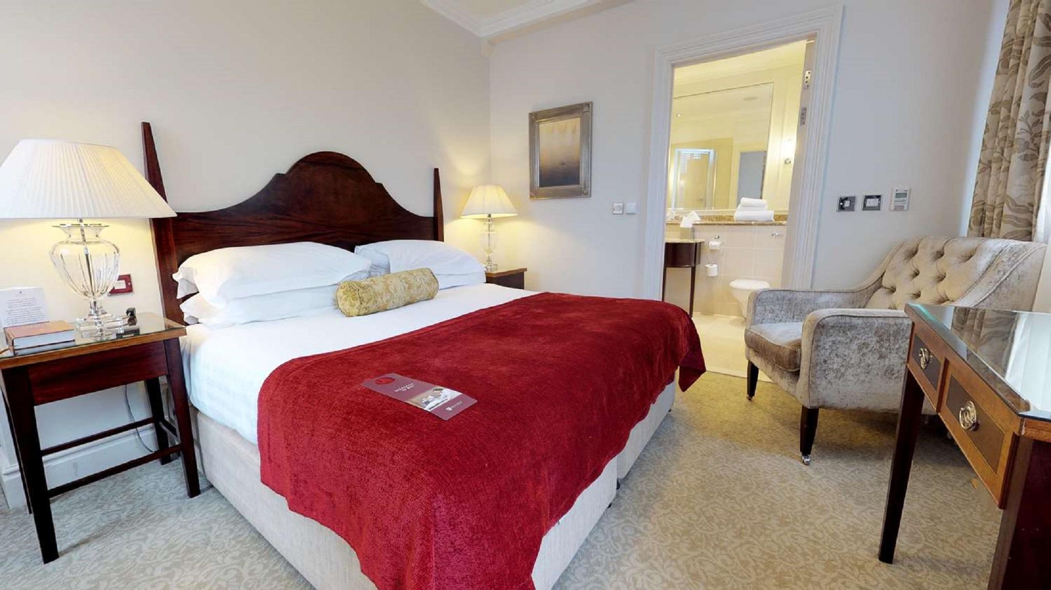 فندق ماكدونالد باث سبا المظهر الخارجي الصورة The photo shows a well-furnished hotel room. In the center, there is a large bed with white linens and a red throw blanket. A decorative pillow is placed on the bed. On either side of the bed, there are bedside tables with lamps. To the right, there 