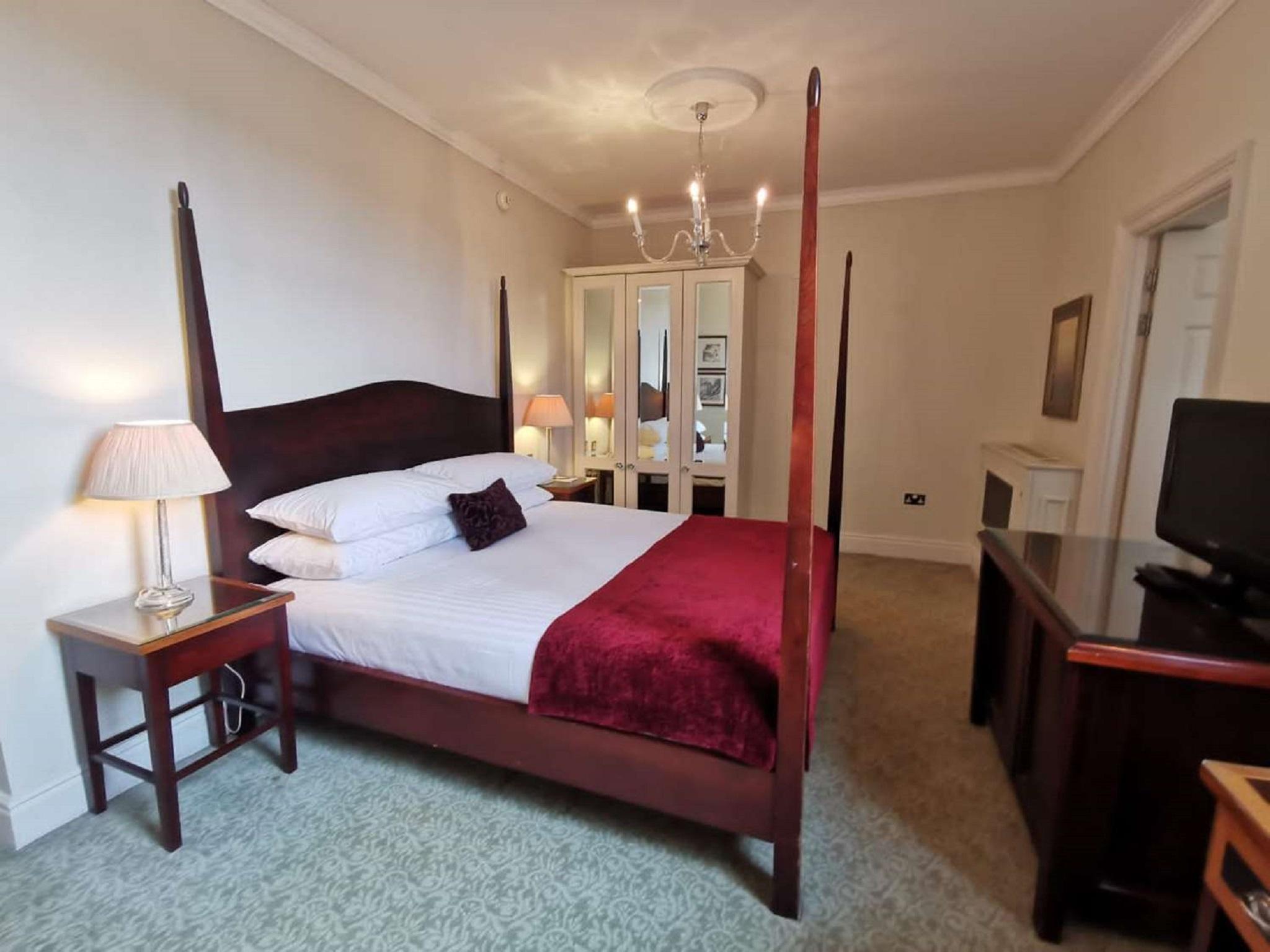 فندق ماكدونالد باث سبا المظهر الخارجي الصورة The photo shows a well-decorated bedroom featuring a four-poster bed with white pillows and a burgundy throw. There are two bedside lamps on wooden nightstands on either side of the bed. A large wardrobe or mirror cabinet is visible in the background