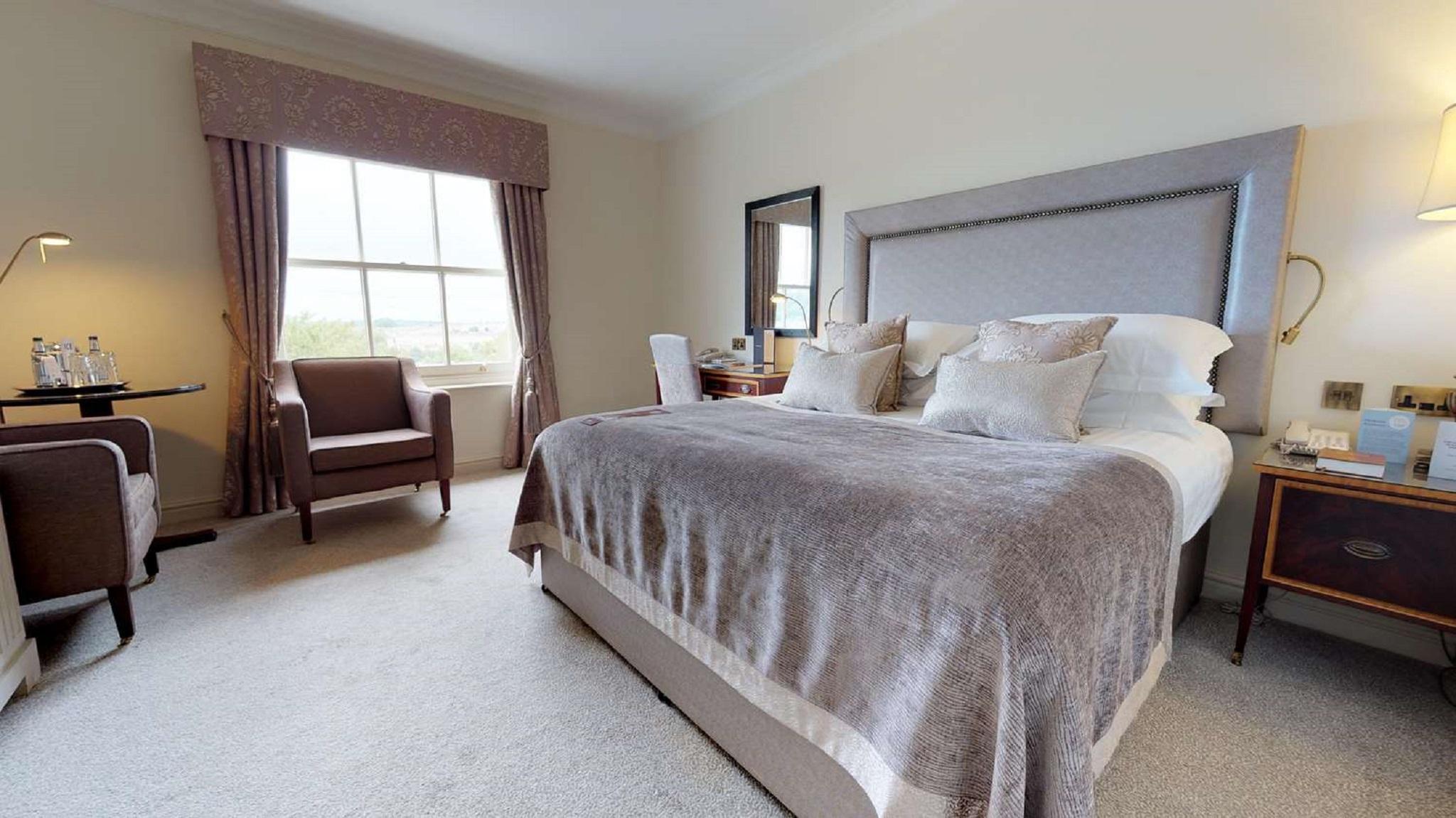 فندق ماكدونالد باث سبا المظهر الخارجي الصورة The photo shows a well-furnished bedroom. It features a large bed with a light gray headboard and several decorative pillows on top. The bed is covered with a soft gray blanket. To one side of the room, there is a comfortable armchair and a small tab