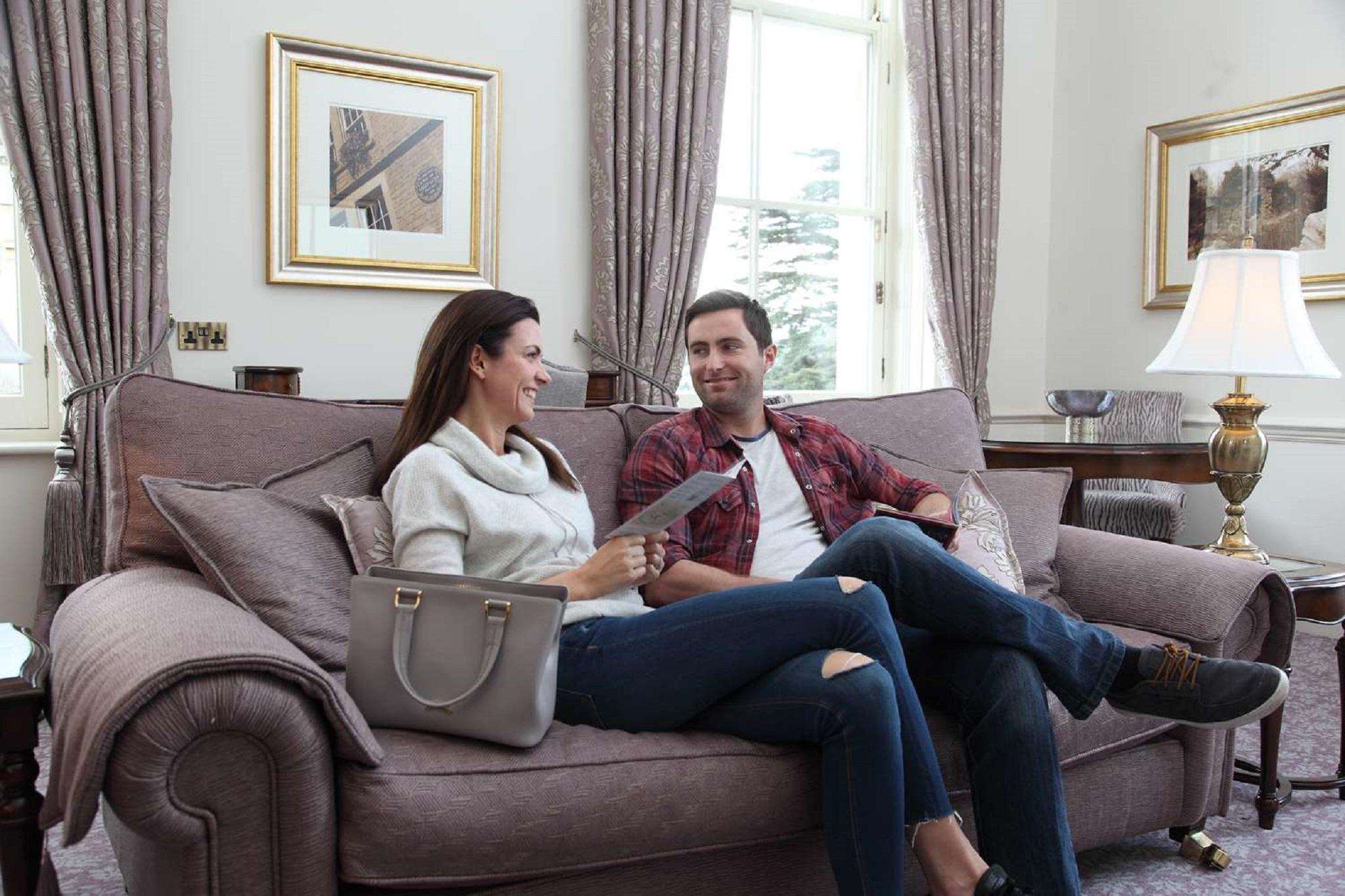 فندق ماكدونالد باث سبا المظهر الخارجي الصورة The photo shows a man and a woman sitting together on a comfortable sofa in a well-decorated room. The woman is holding a piece of paper and appears to be engaged in conversation with the man, who is smiling in response. They are both dressed casuall