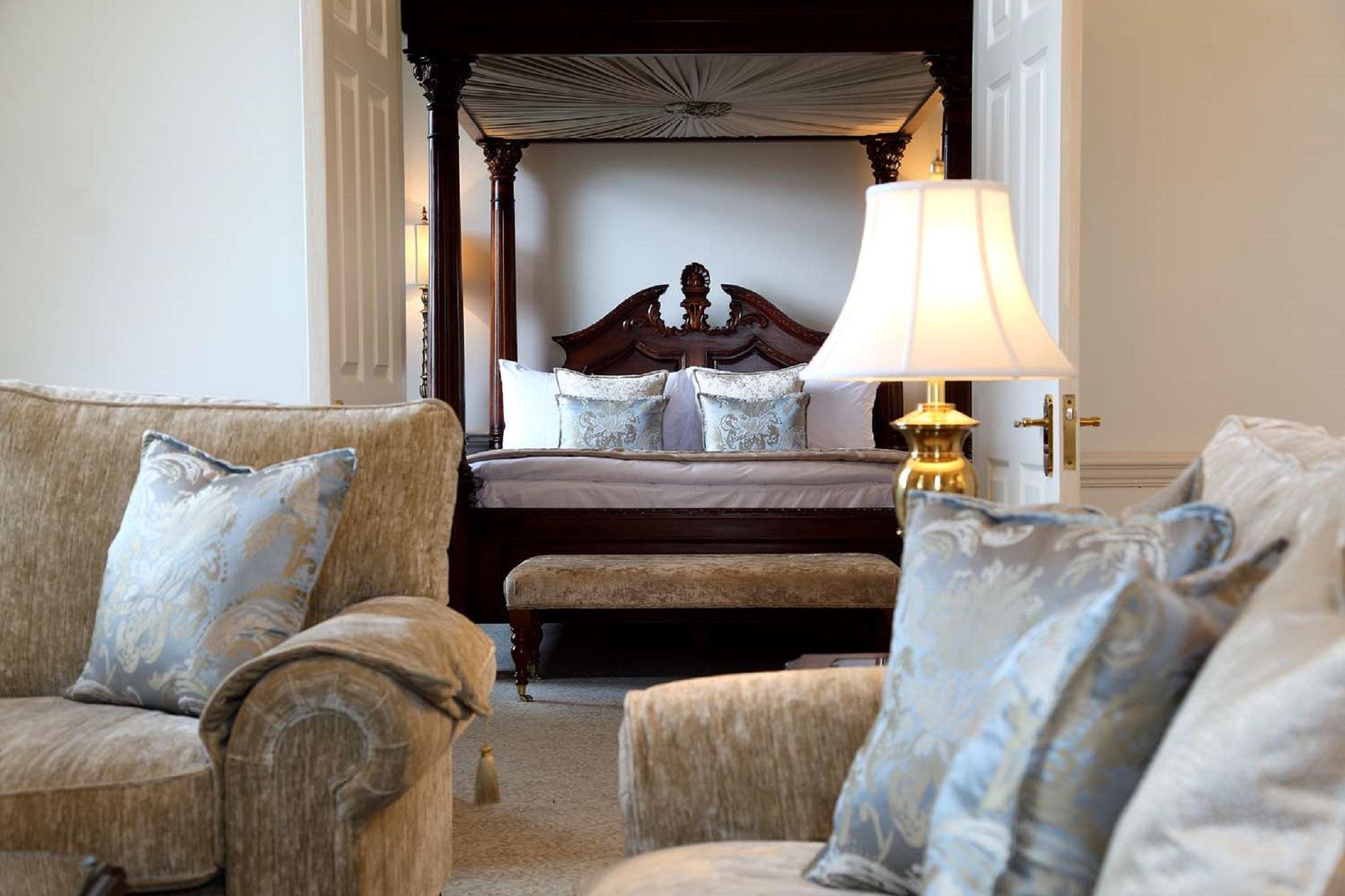 فندق ماكدونالد باث سبا المظهر الخارجي الصورة The photo shows a beautifully decorated room featuring a four-poster bed in the background. The bed has a wooden frame with a rich design, and it is adorned with plush bedding and pillows. In the foreground, there are comfortable sofas with decorativ