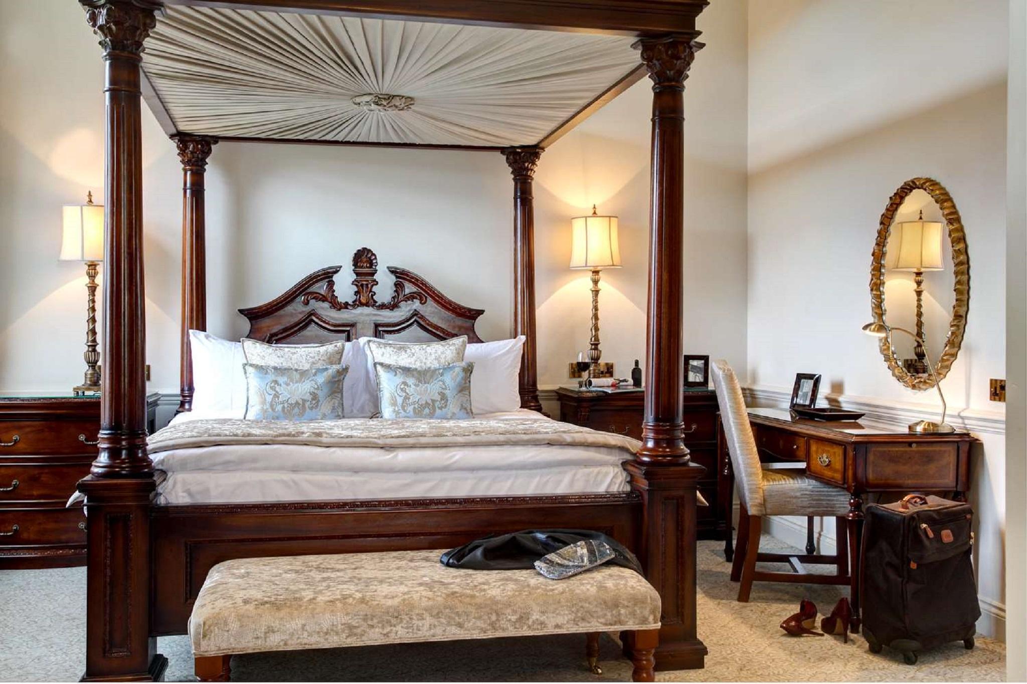 فندق ماكدونالد باث سبا المظهر الخارجي الصورة The photo showcases a beautifully designed bedroom featuring a four-poster canopy bed with intricate woodwork and elegant drapery. The bed is adorned with plush pillows and a decorative bedspread. On either side of the bed, there are stylish lamps il