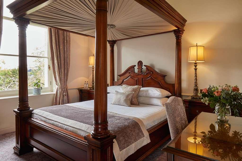 فندق ماكدونالد باث سبا الغرفة الصورة The photo shows a beautifully designed bedroom featuring a four-poster bed made of dark wood. The bed has an elaborately carved headboard and is adorned with a light-colored bedding set. Above the bed, there is a canopy that adds an elegant touch. On